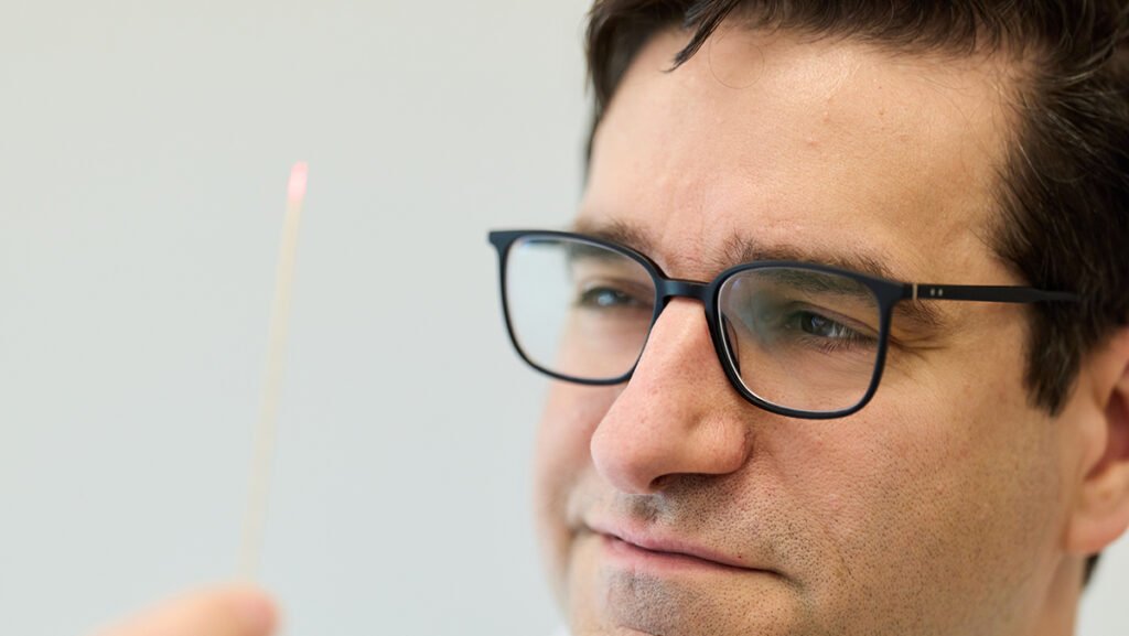 A person wearing glasses holds a thin stick with a small pink tip, looking at it intently.